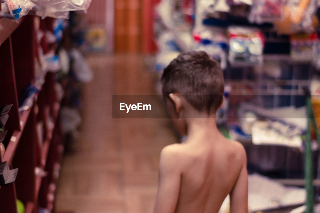 Rear view of shirtless boy by shelves