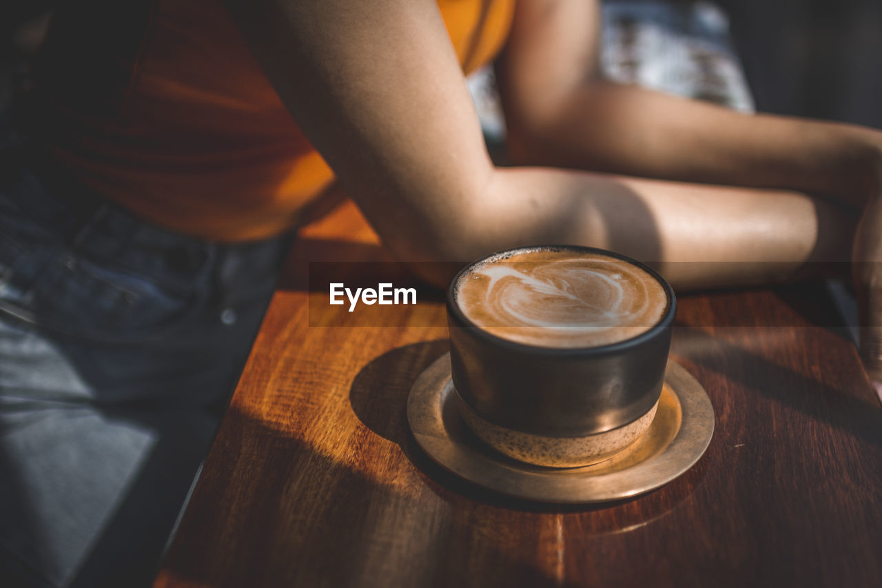 Midsection of woman with coffee cup at table