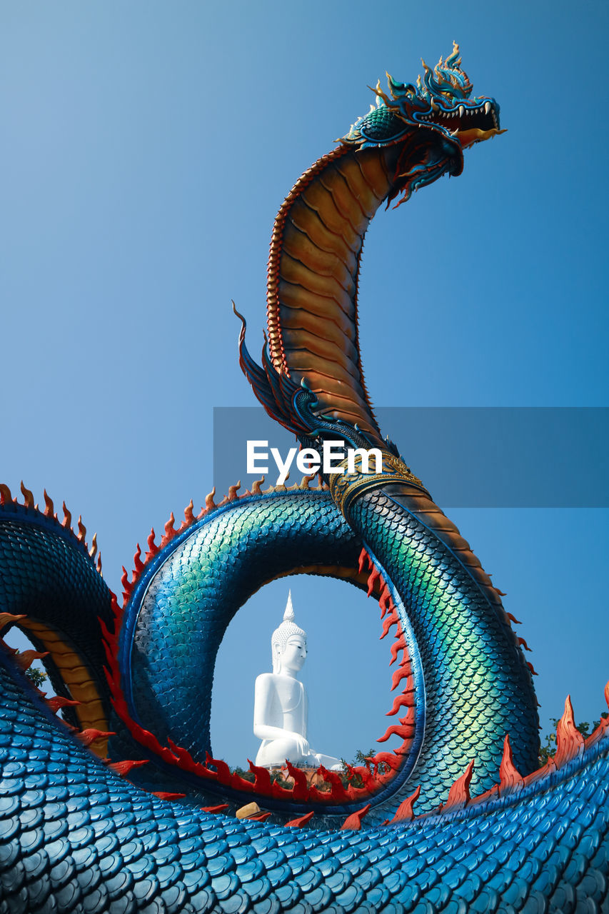 Low angle view of dragon and buddha statue against blue sky