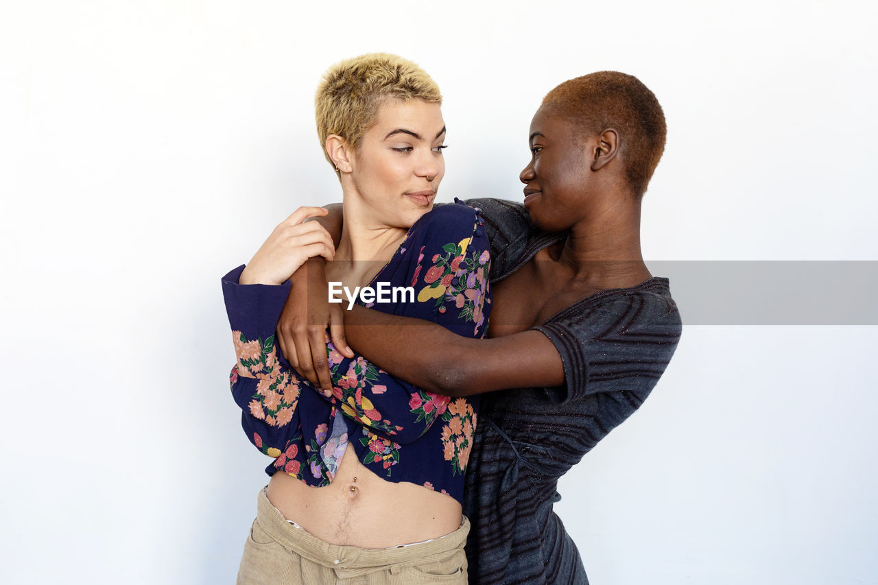 Lesbian couple embracing while standing against white background