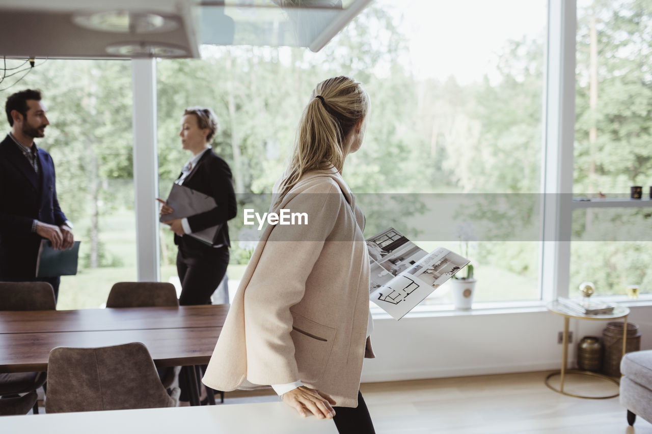 Female with magazine looking through window while partner consulting real estate agent at new property