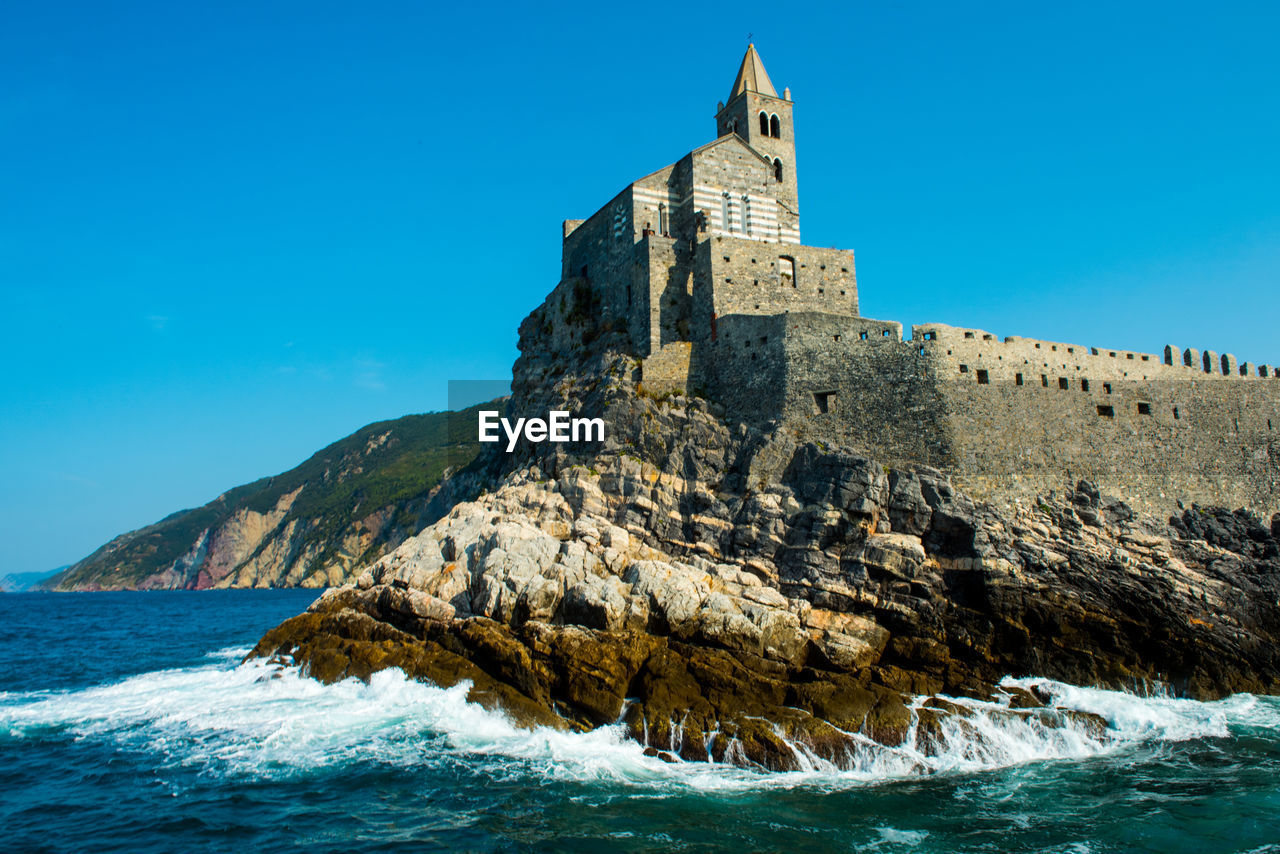 Low angle view of castle by sea against clear blue sky