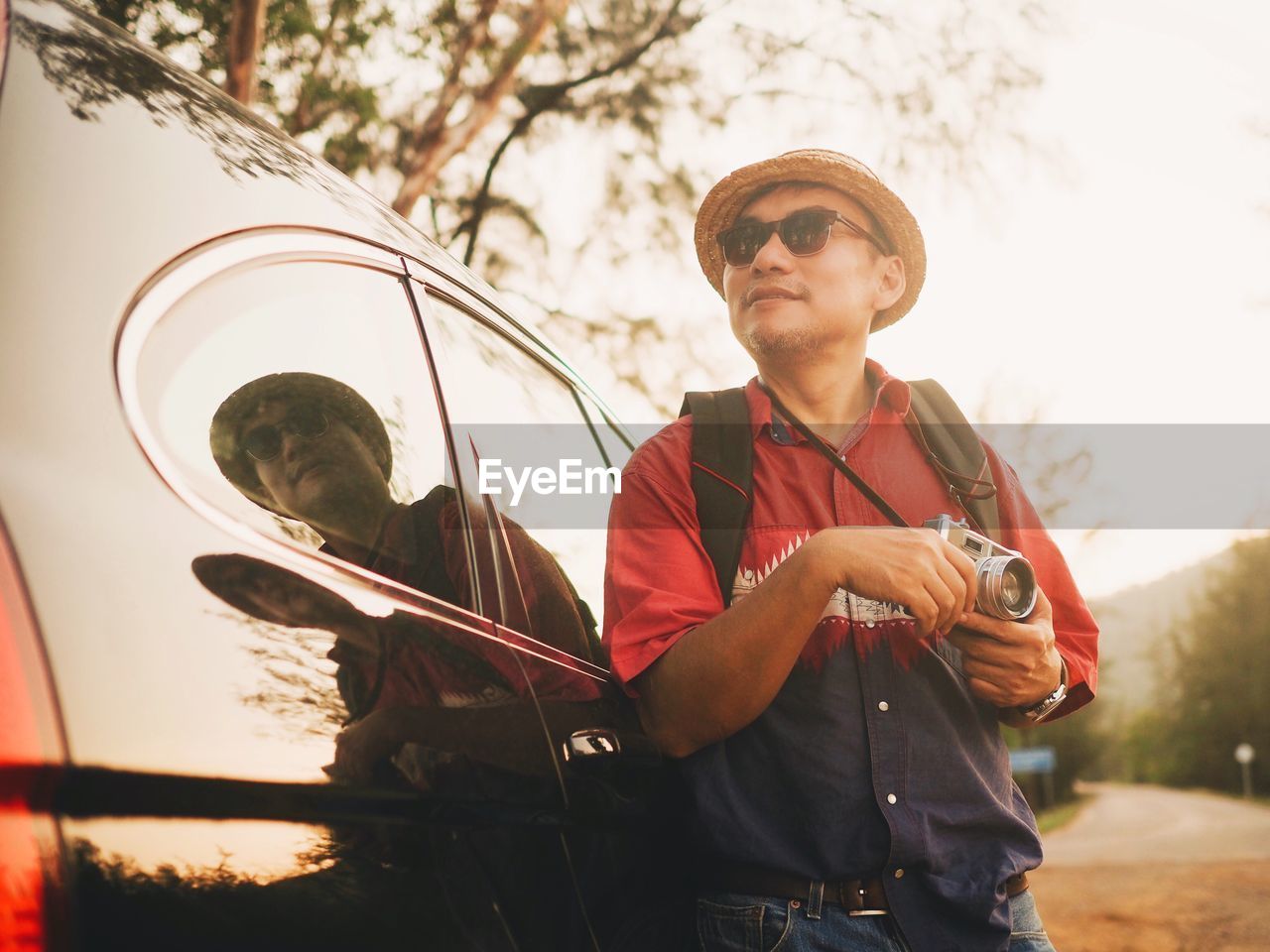 Man in sunglasses holding camera while standing by car