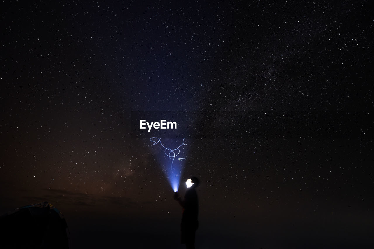 Low angle view of silhouette man standing against star field at night