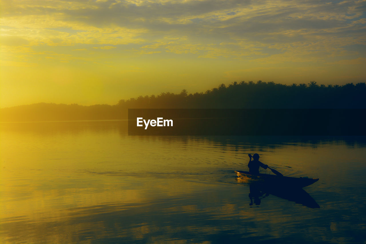 SILHOUETTE PERSON IN BOAT ON LAKE AGAINST SKY DURING SUNSET