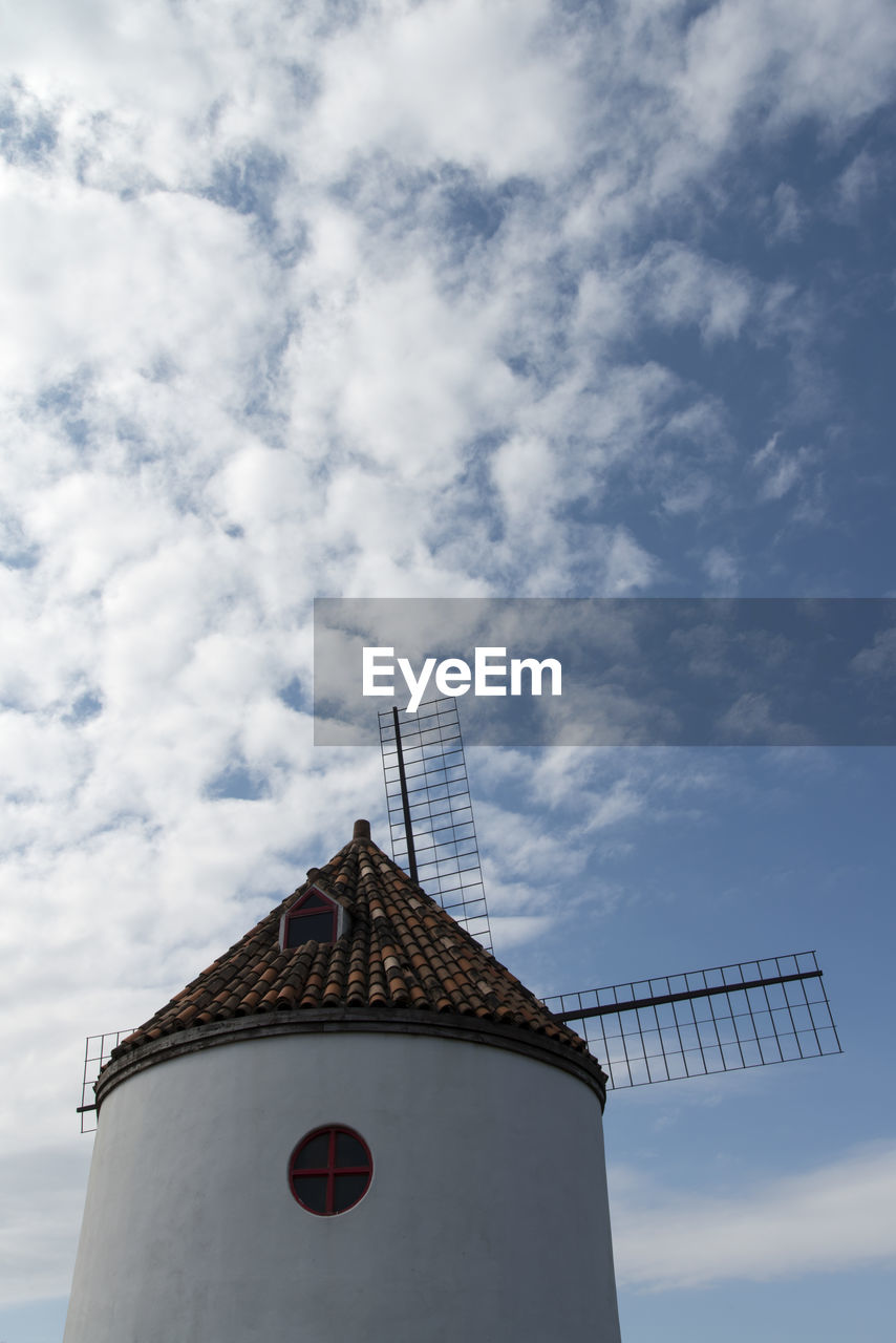 Low angle view of traditional windmill against cloudy sky