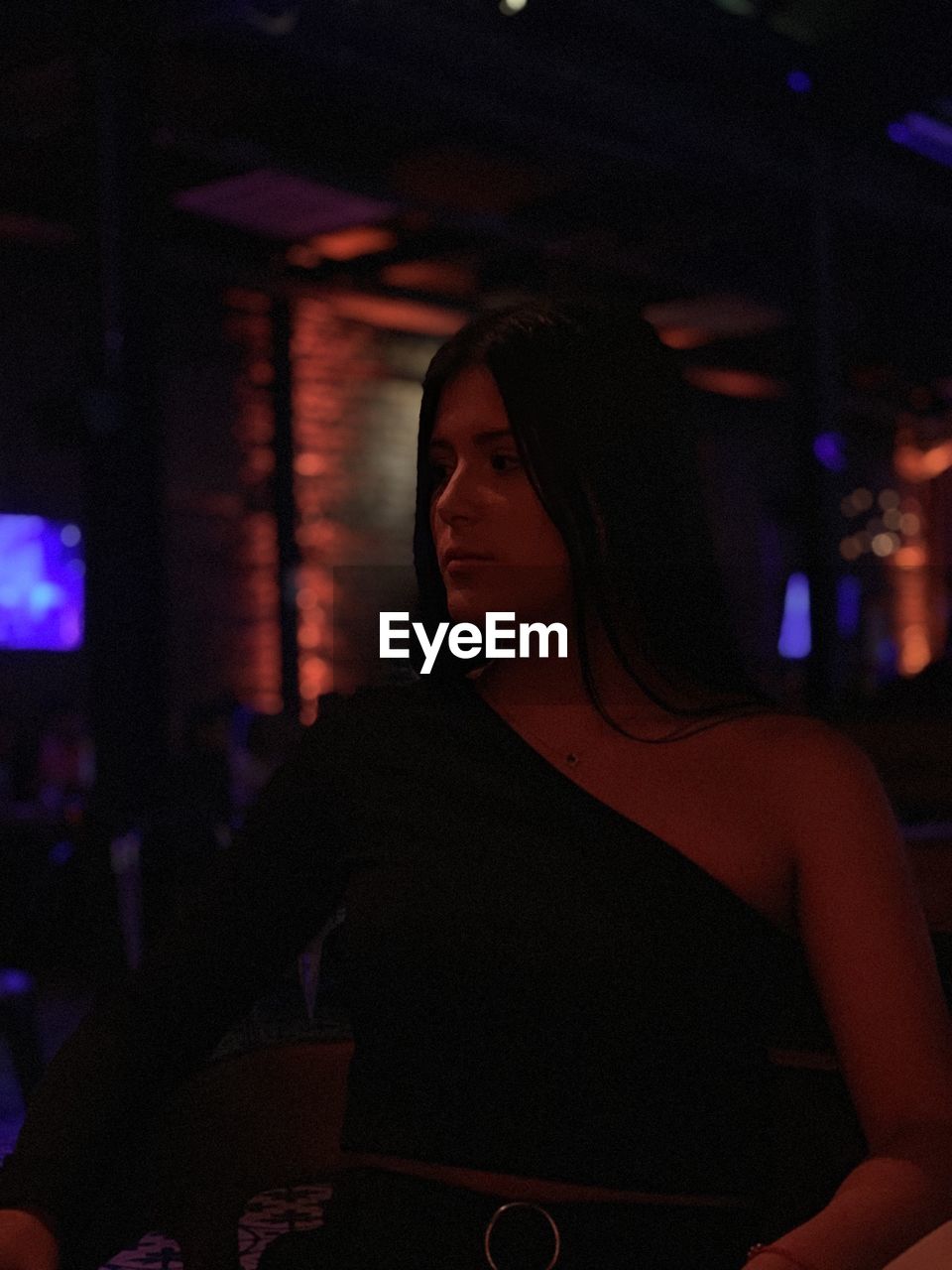 Young woman looking away while standing at illuminated restaurant