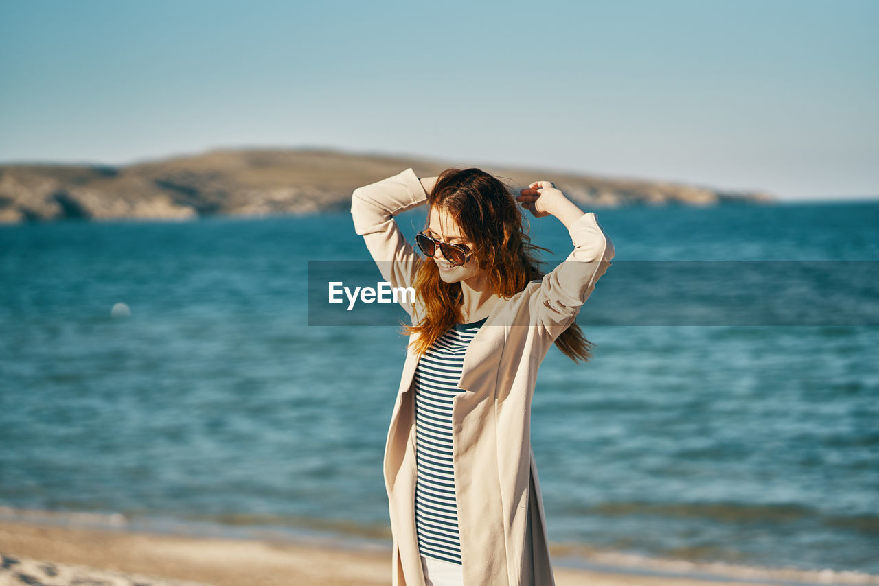 WOMAN STANDING BY SEA AGAINST SKY