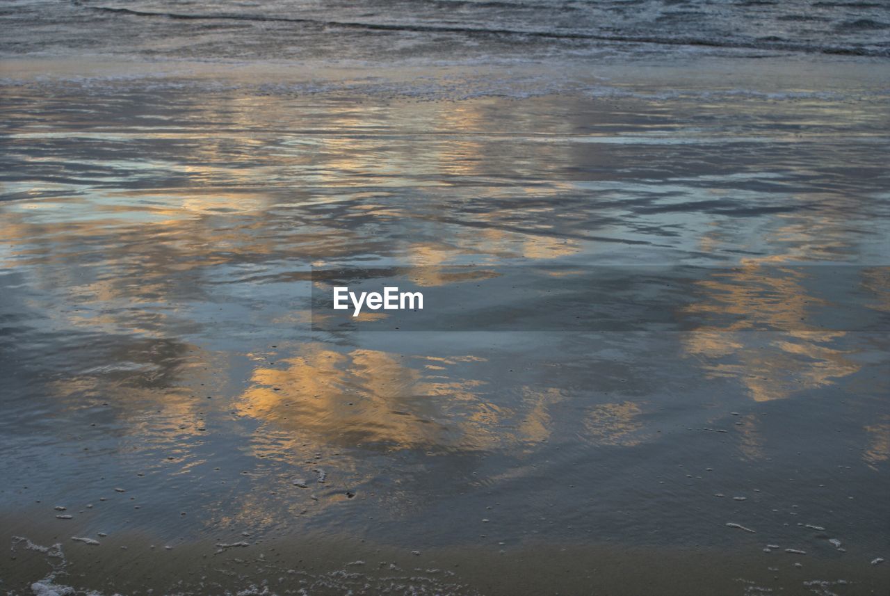 Reflection of cloudy sky on wet sand at beach