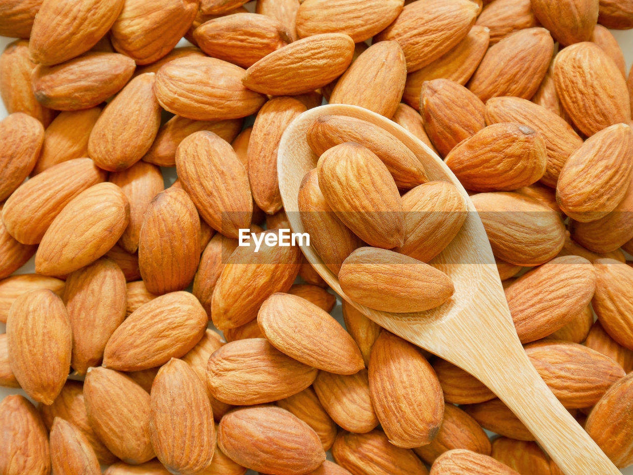 Almonds in wooden spoon on piles of almonds