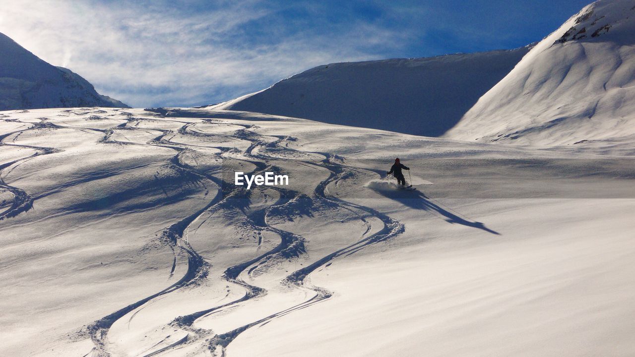 Rear view of person skiing on snow covered mountain against blue sky