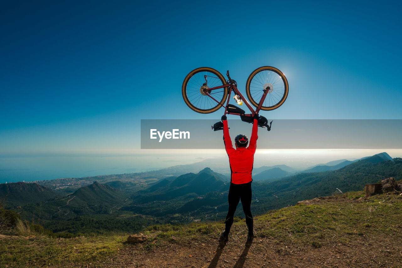Succesful adult male cyclist rises his bicycle over his head on top of a mountain