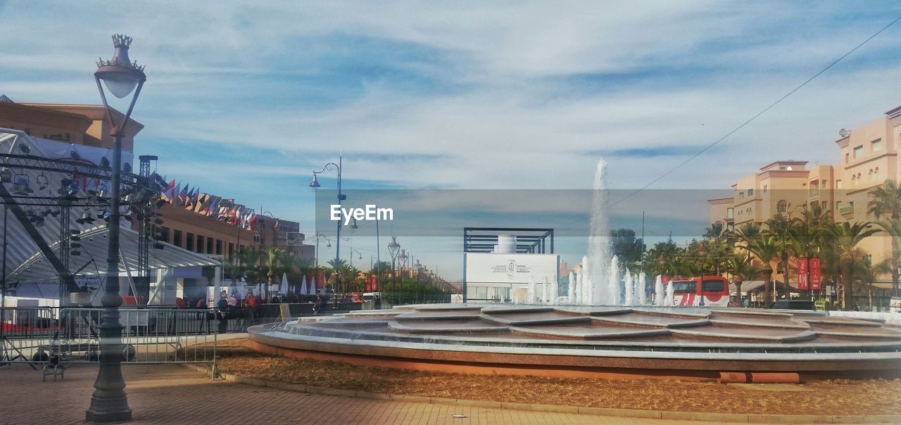 Fountain by buildings against cloudy sky