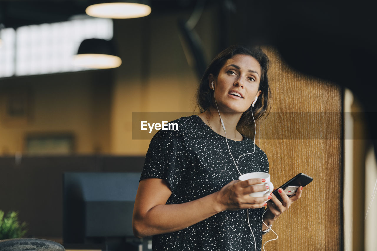 Female computer programmer with earphones talking on smart phone in creative office