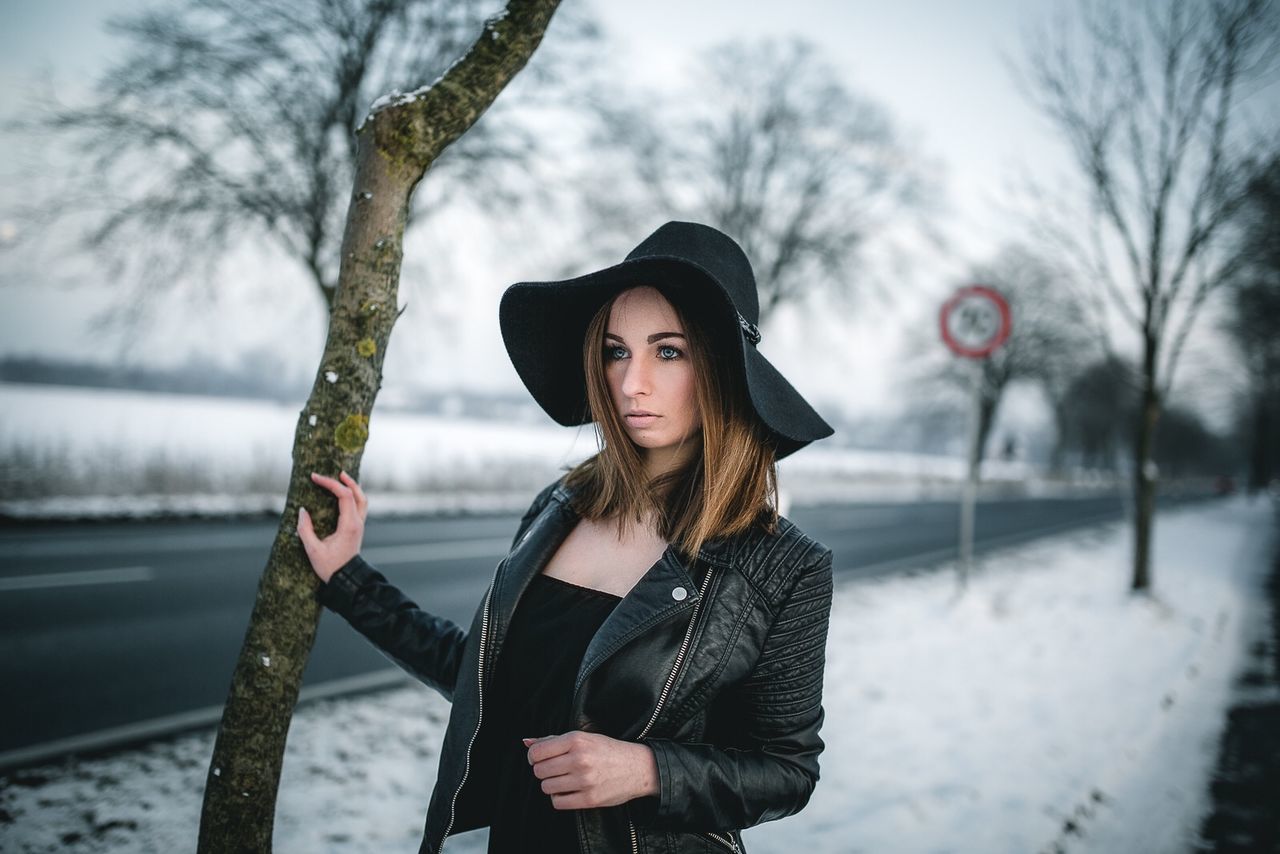 PORTRAIT OF YOUNG WOMAN STANDING ON TREE TRUNK