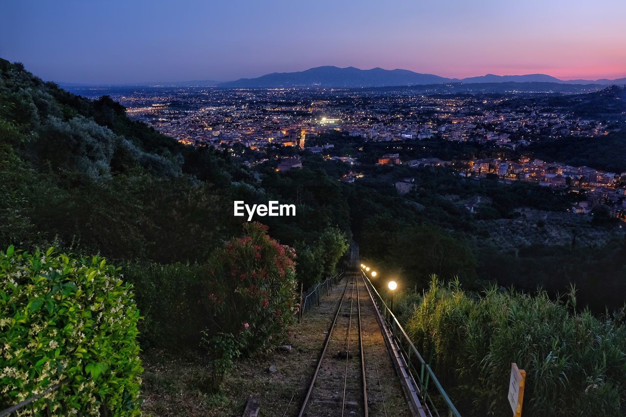 HIGH ANGLE VIEW OF RAILROAD TRACKS BY MOUNTAIN AGAINST SKY AT NIGHT