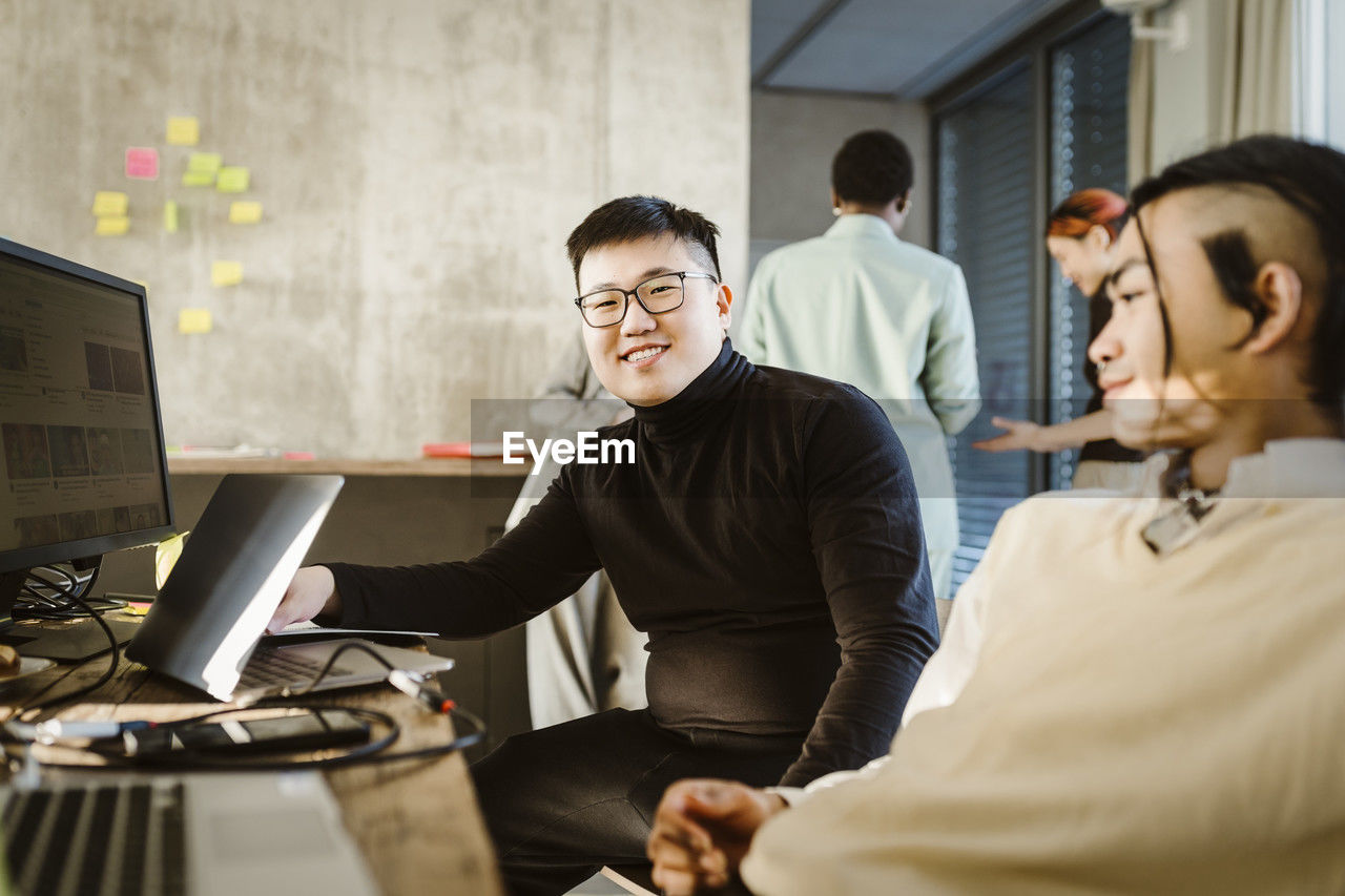 Portrait of smiling programmer sitting with colleague at desk in creative office