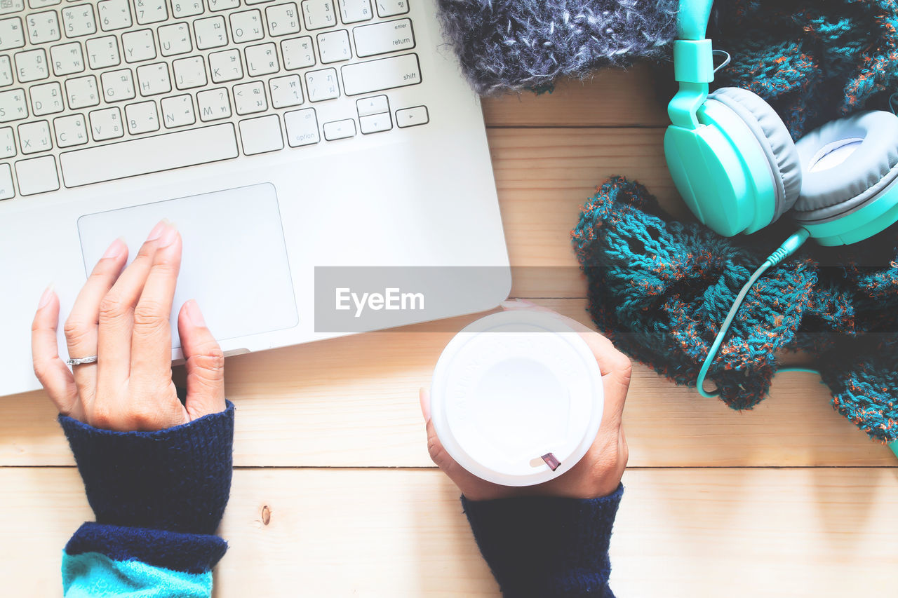 Directly above shot of cropped hand using laptop while holding coffee cup at table