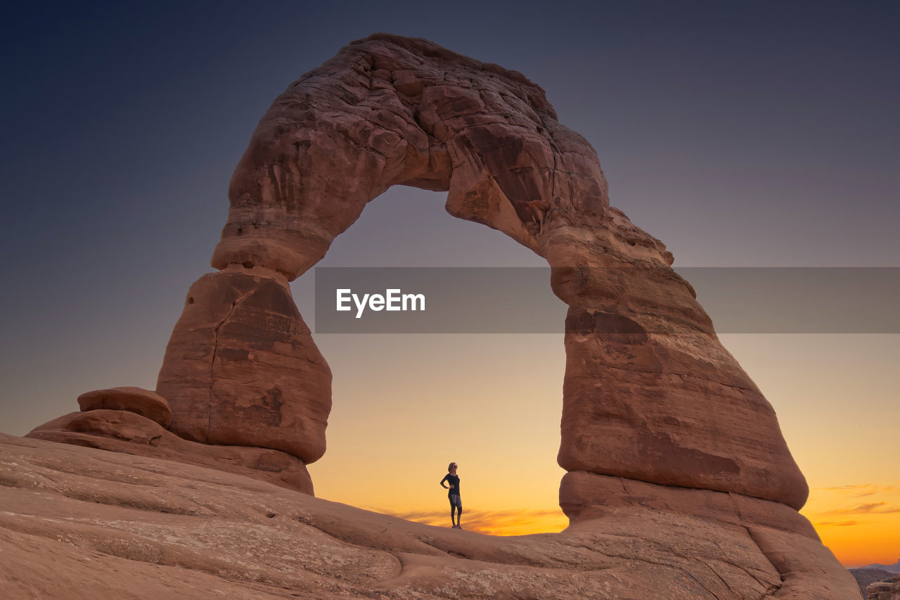 MAN STANDING ON ROCK FORMATION AGAINST SKY