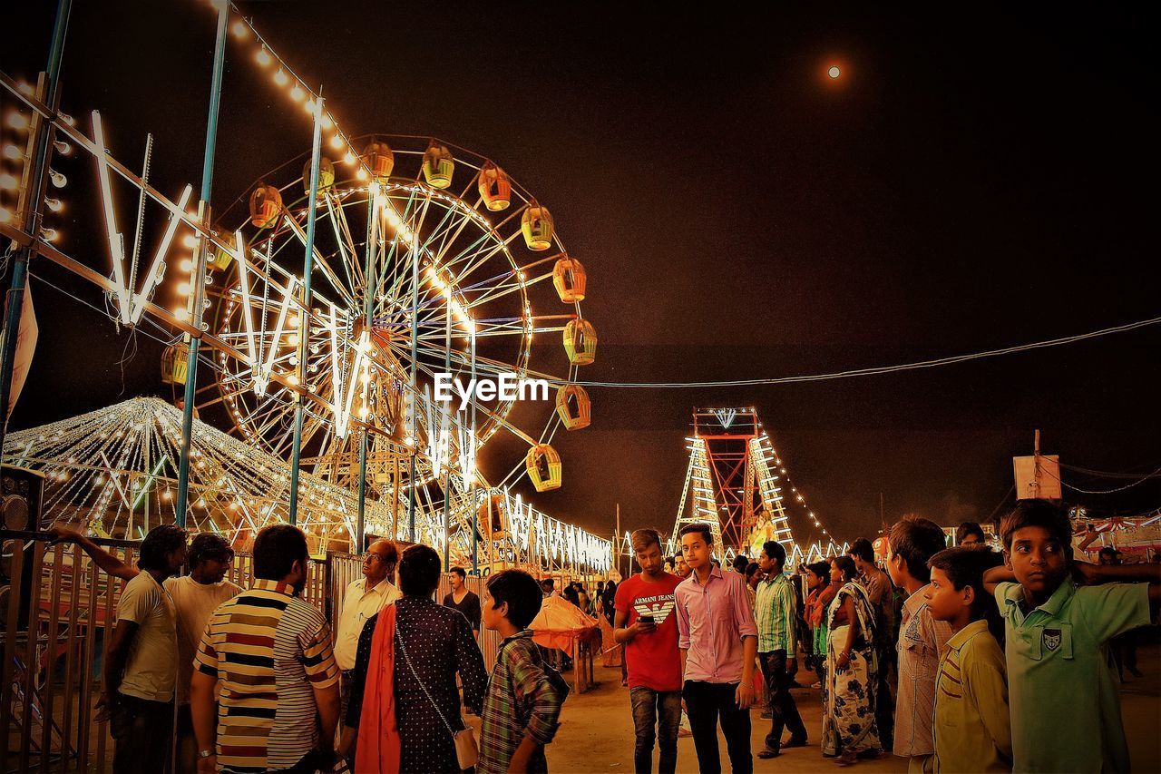 People in amusement park against sky at night