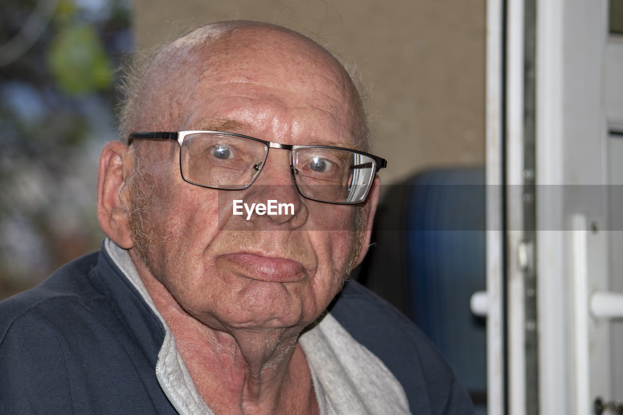 Old grandfather with glasses is bald. looks into the camera on a sunny autumn day.