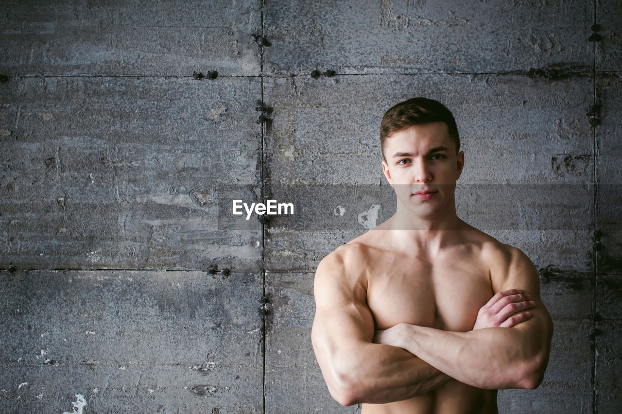 Close-up portrait of shirtless muscular man standing by wall