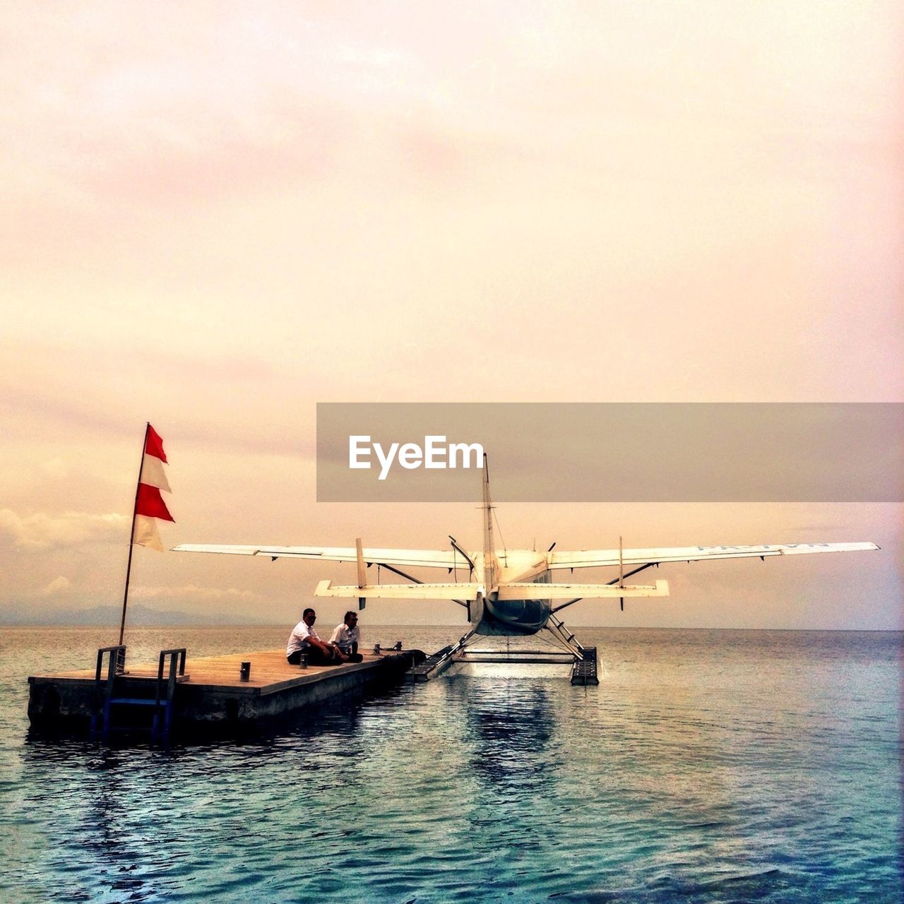 Men sitting on pier by float plane on sea against sky