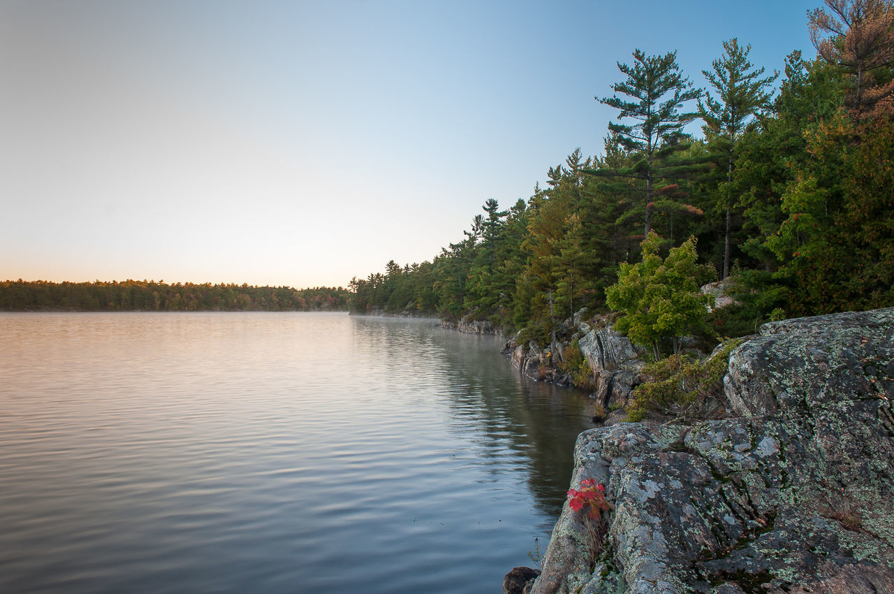 Lake with rocks an trees against clear sky