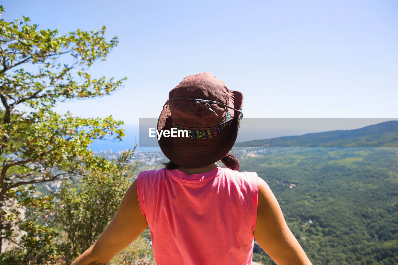 Woman in a hat looks at the panoramic view from the mountain to the sea and the 