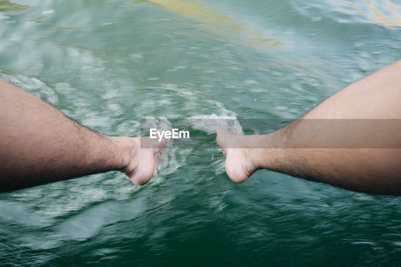 Low section of man touching sea