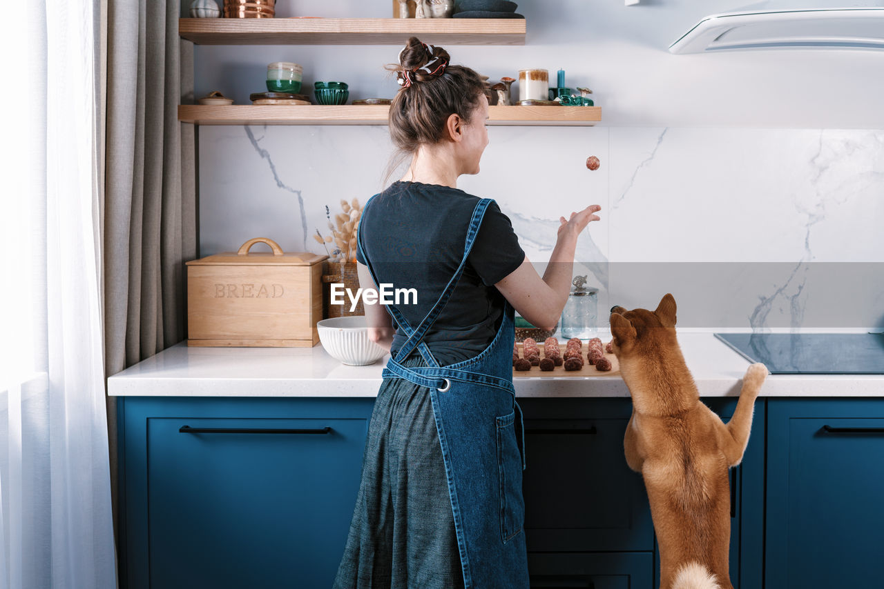 Funny woman cooking meatballs with her furry friend shiba inu dog. cooking at home 