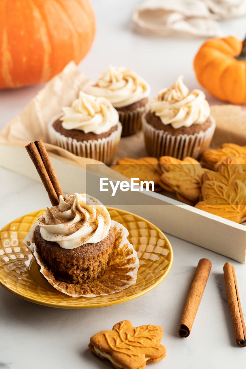 A tray of pumpkin spice cupcakes and cookies with a cupcake on a plate in front.