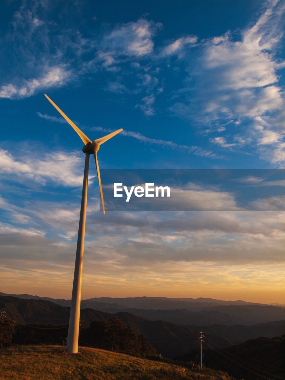 WINDMILLS ON FIELD AGAINST SKY DURING SUNSET