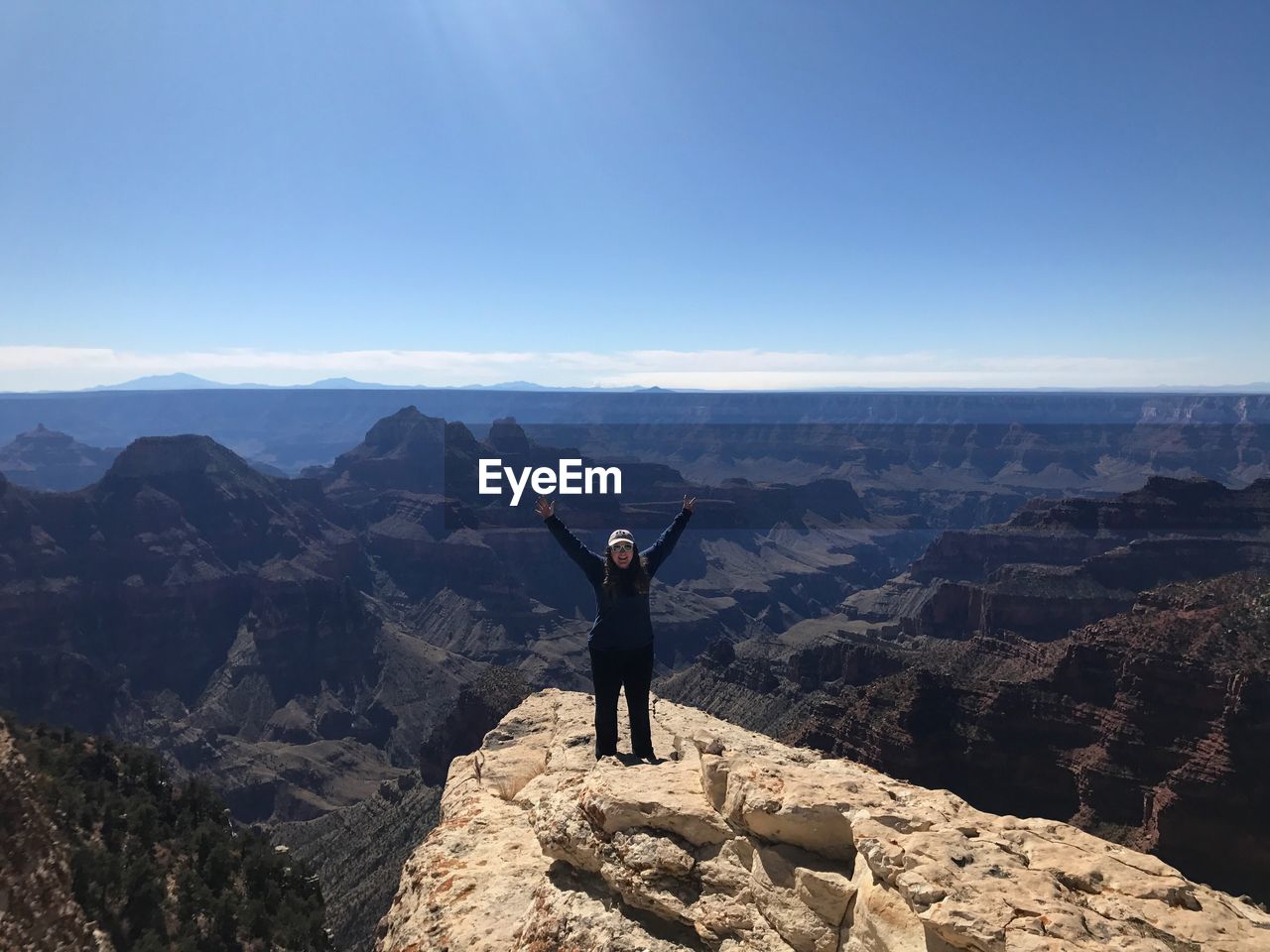 Full length of hiker with arms raised standing on mountain against sky