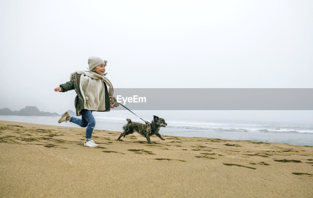 Happy girl running with dog on the beach on a foggy winter day