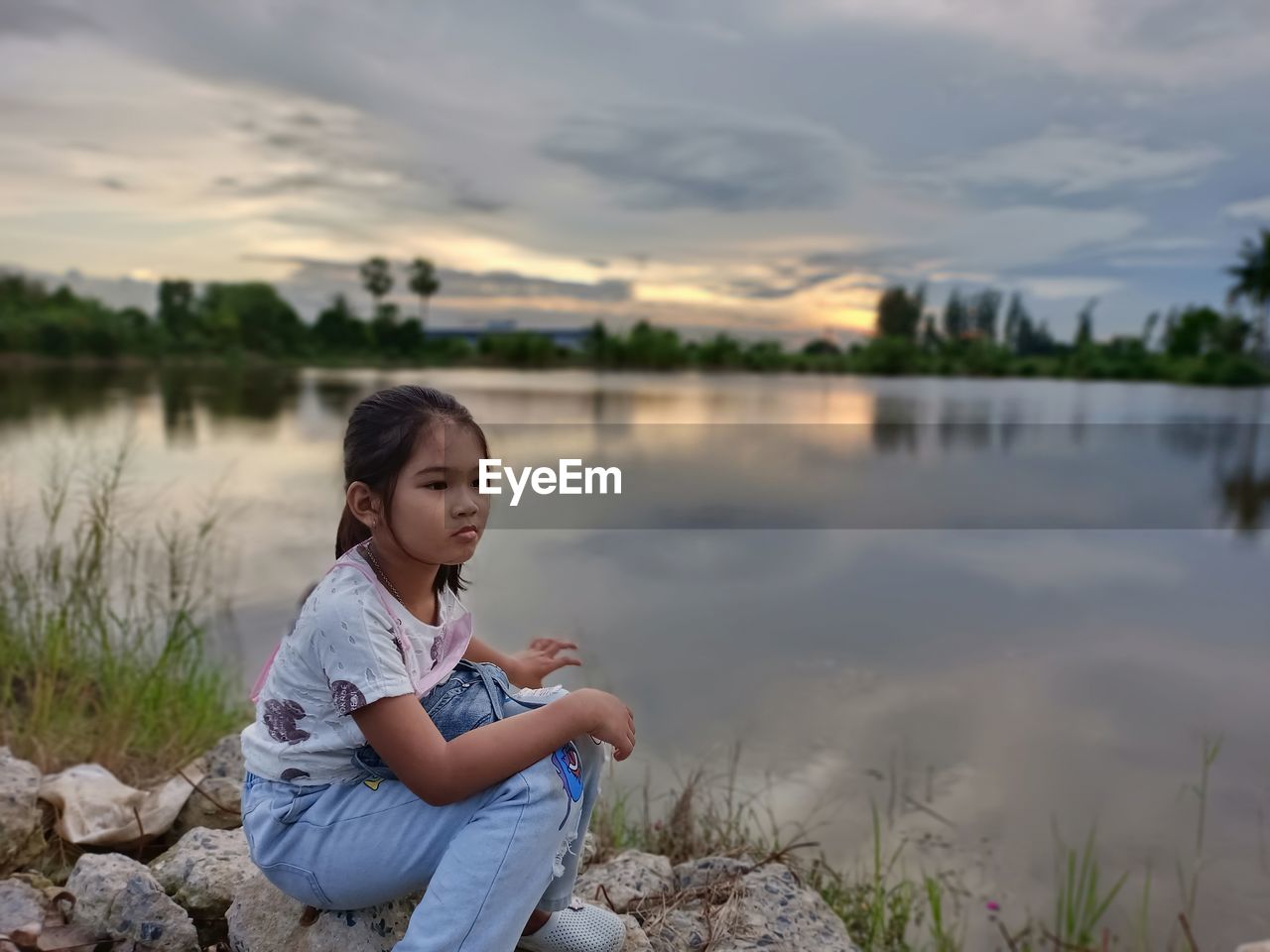 GIRL SITTING ON LAKE AGAINST SKY