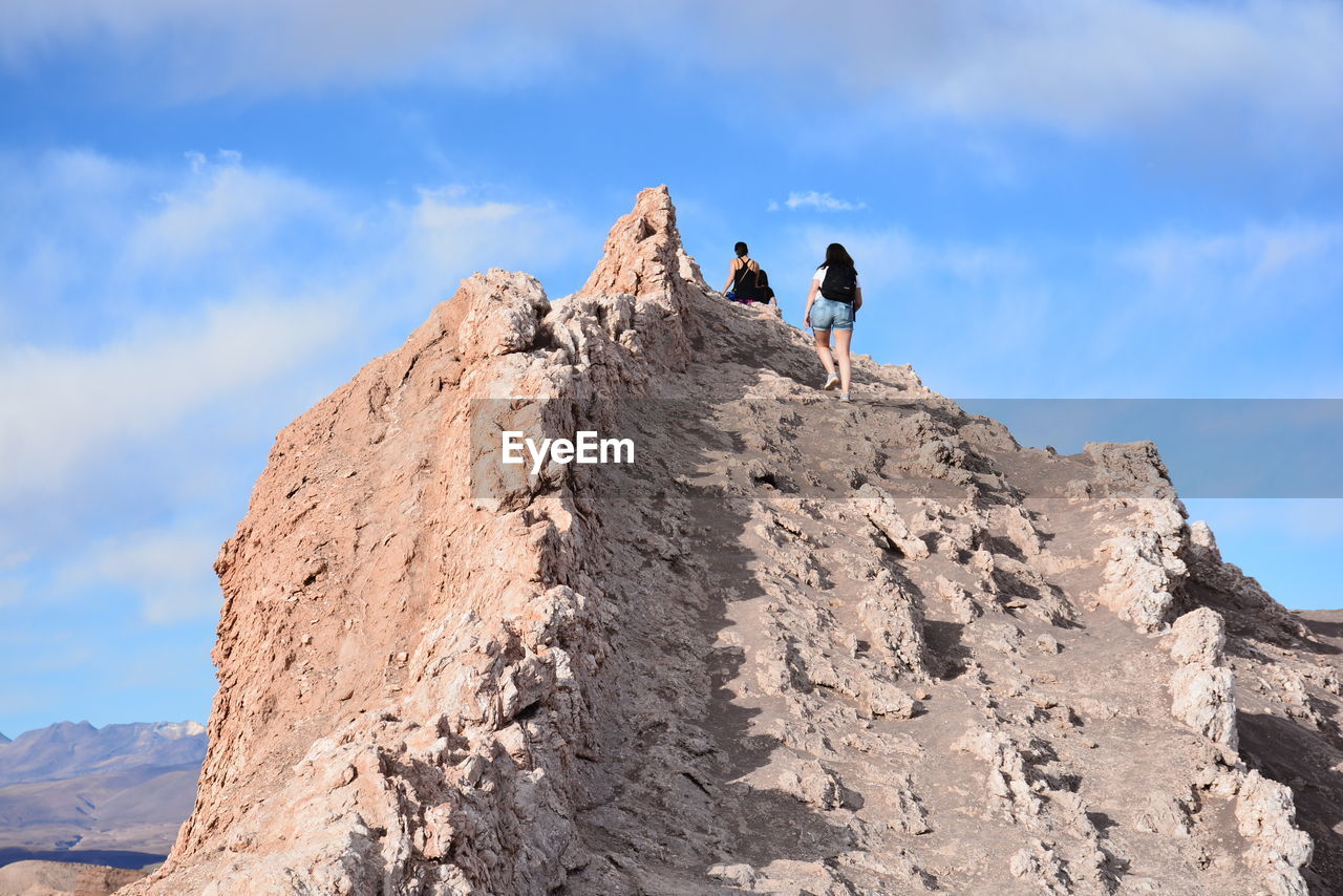 LOW ANGLE VIEW OF FRIENDS ON MOUNTAIN AGAINST SKY