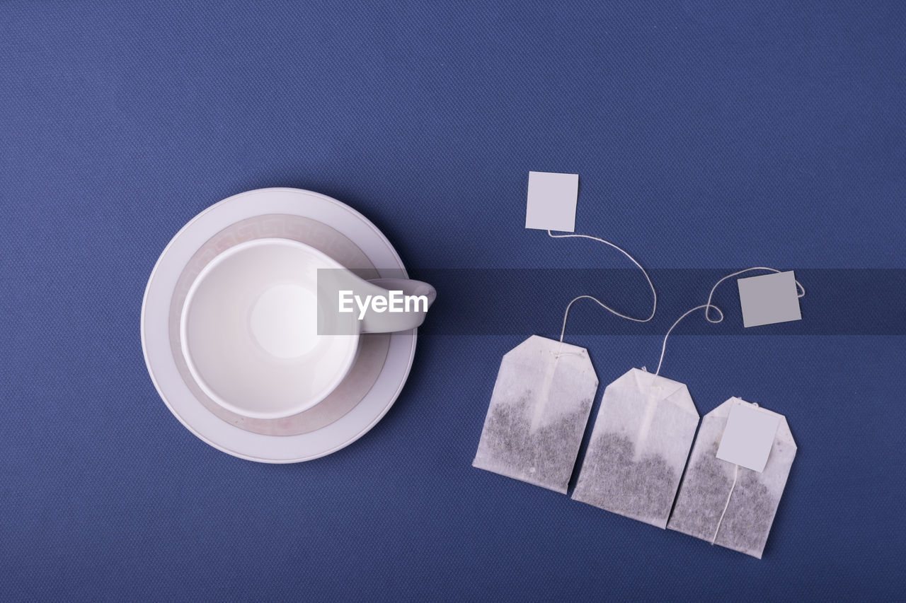 Empty porcelain white cup with three teabags on dark blue background. top view studio shot