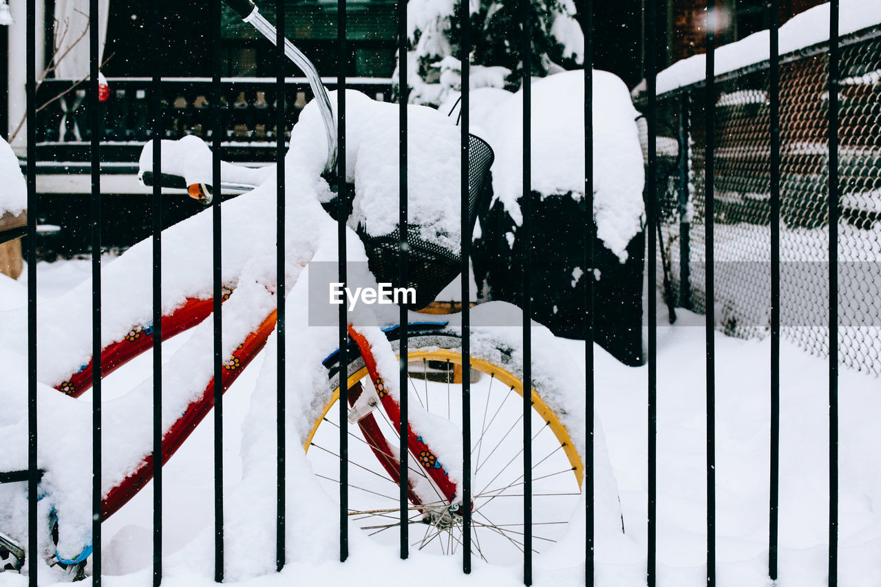 Snow covered bicycle seen through fence