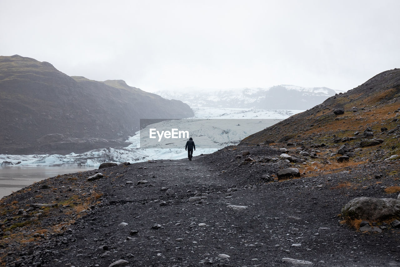 Rear view of man walking on mountain against sky