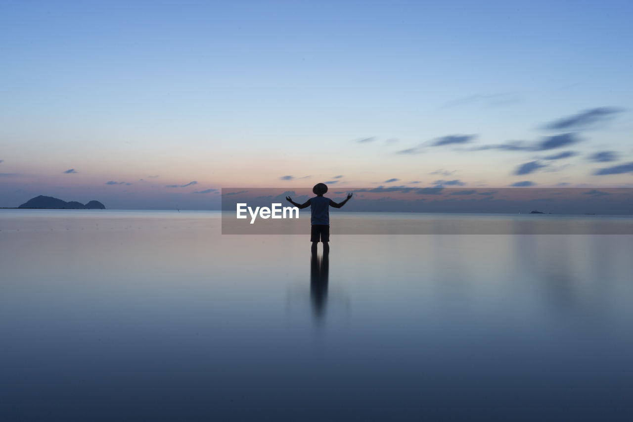 Silhouette man standing in sea against sky during sunset