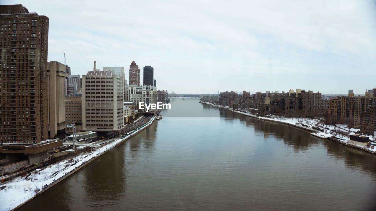 Cityscape amidst river against sky during winter