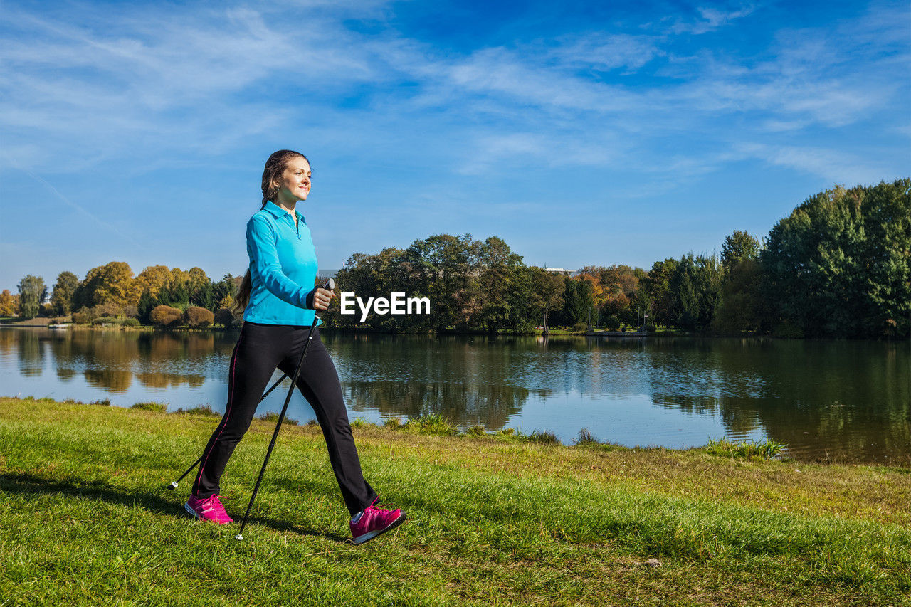 side view of woman exercising at lakeshore against sky