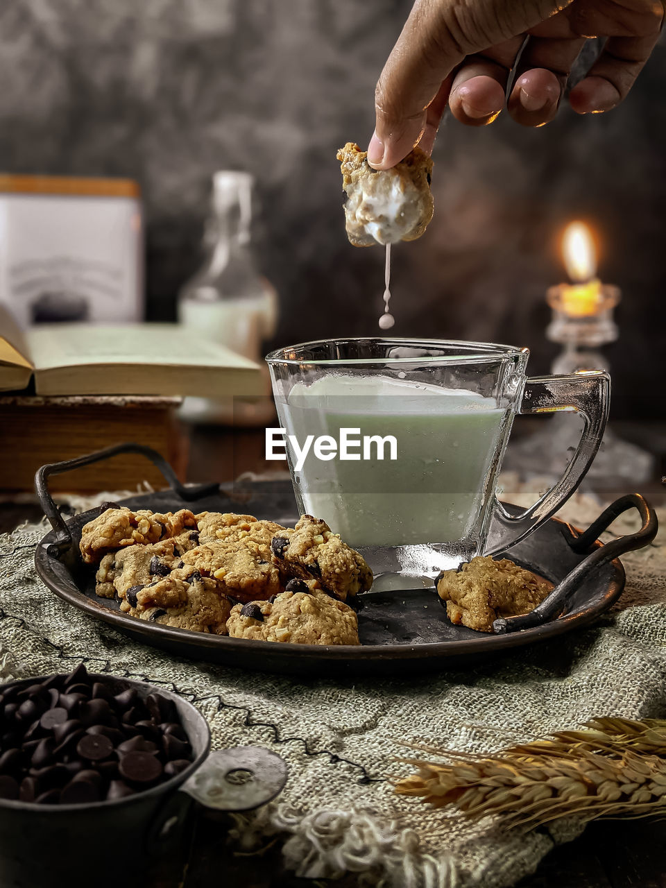 Cropped hand of person dipping a cookies in a glass of milk on table