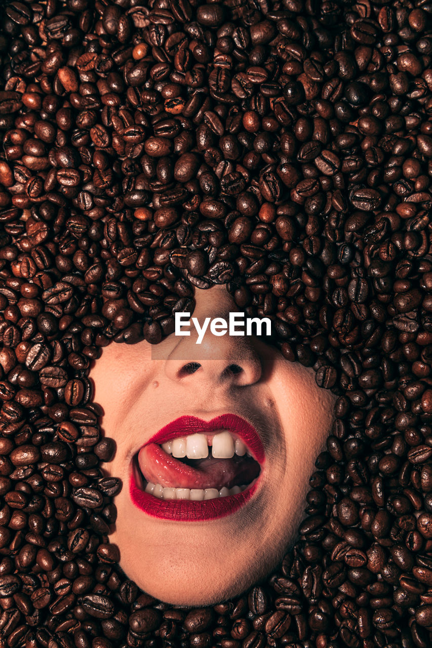 Face of a young, passionate female covered with coffee beans.