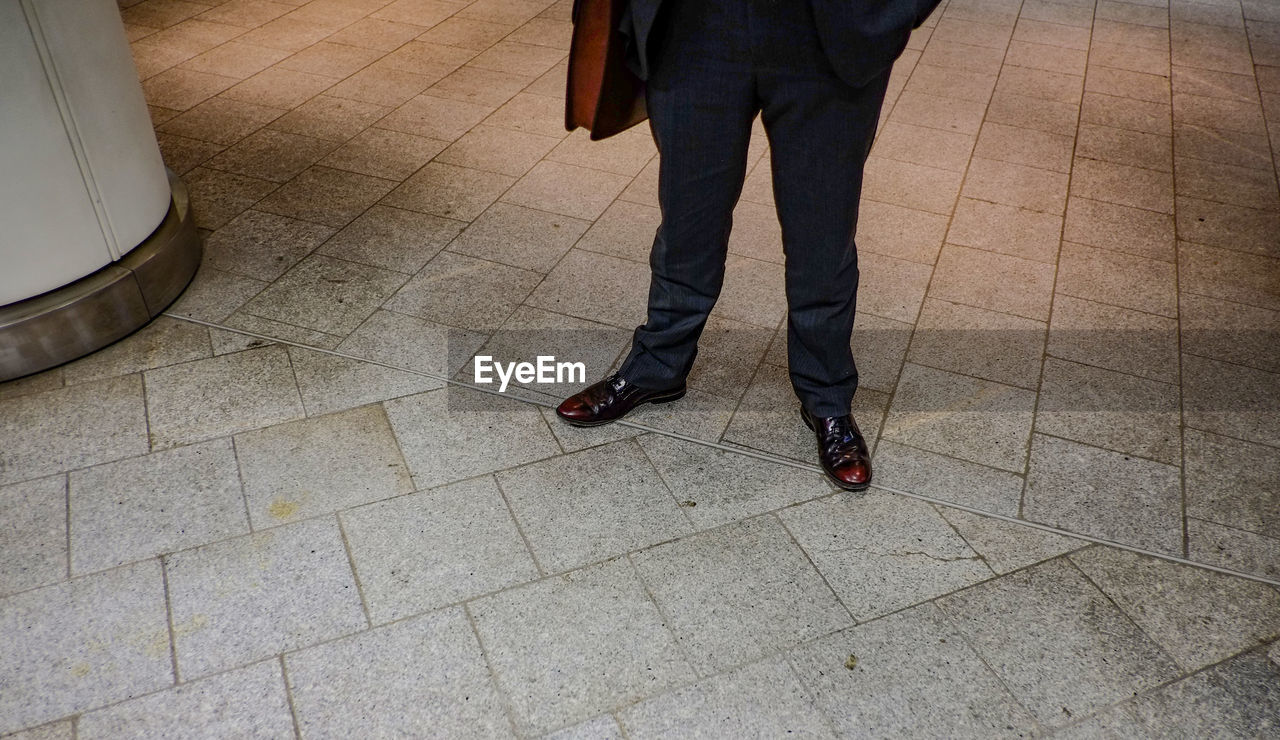 LOW SECTION OF MAN STANDING ON TILED FLOOR