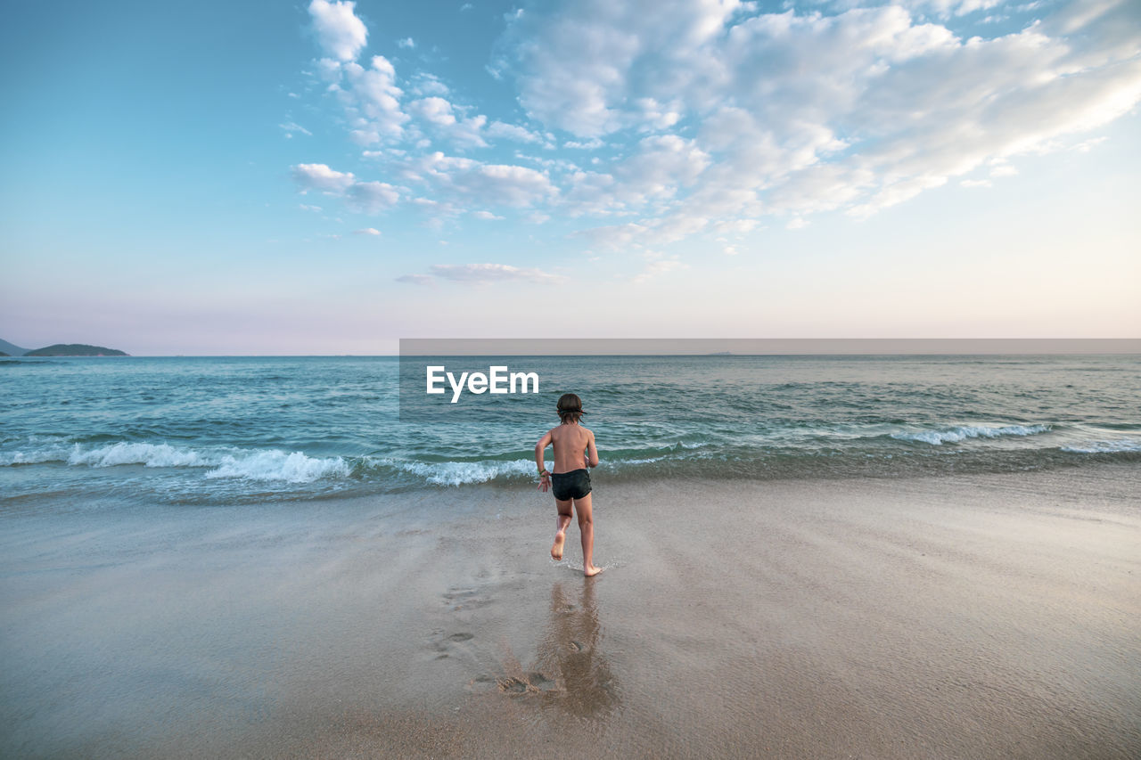 Baxk view of 5 years old kid running towards the ocean