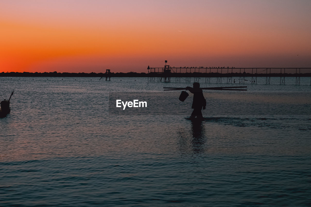 SILHOUETTE PEOPLE ON BEACH AGAINST ORANGE SKY