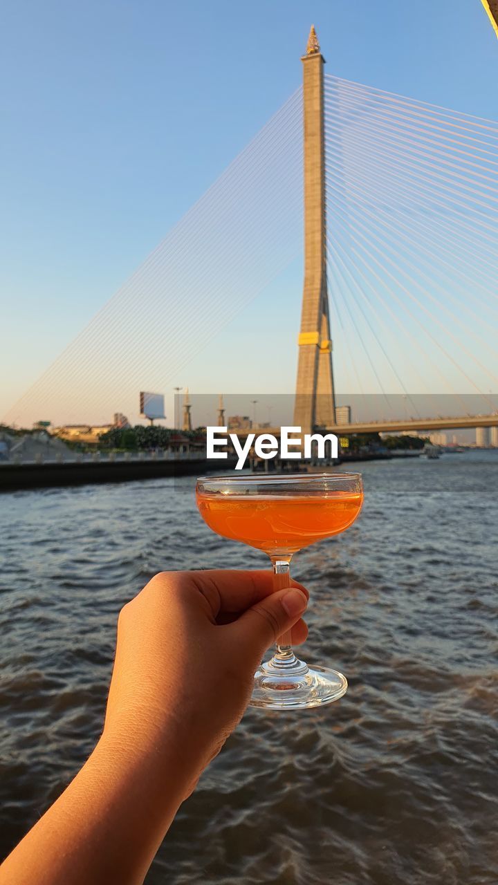 A hand is holding a glass of cocktail with beautiful view of bangkok and chaophraya river. 