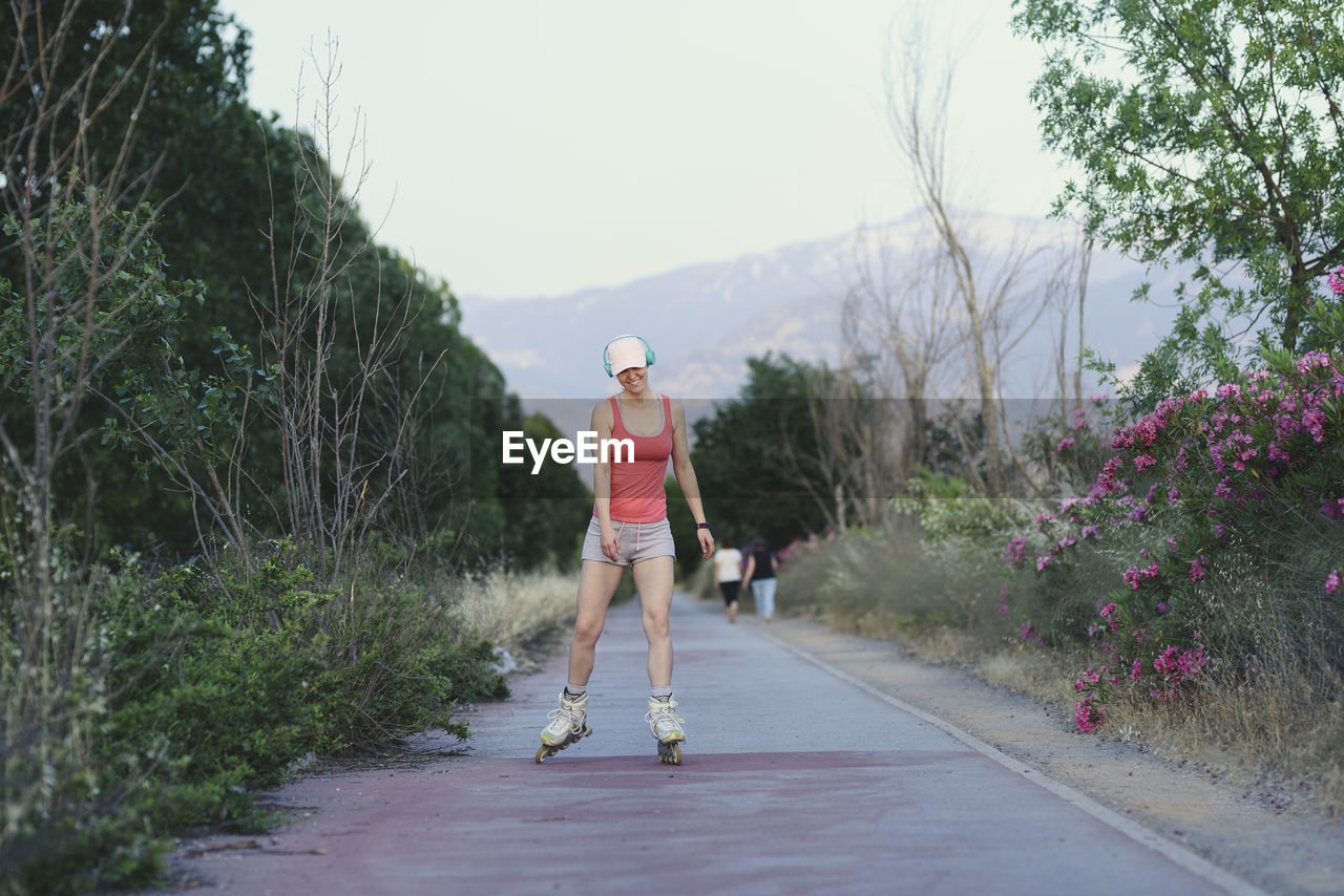 WOMAN ON ROAD BY TREES AGAINST SKY